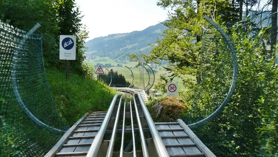 Blick aus Fahrerperspektive auf die Schienen des Alpsee Coasters mit Fangnetzbögen, im Hintergrund Berge